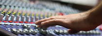Photo of a hand controlling a sound board in a studio